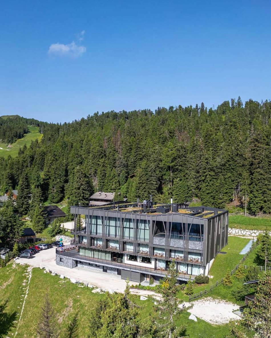 Il tuo hotel in Val Pusteria: Olangerhof Hotel moderno tra alberi e montagne con cielo blu limpido