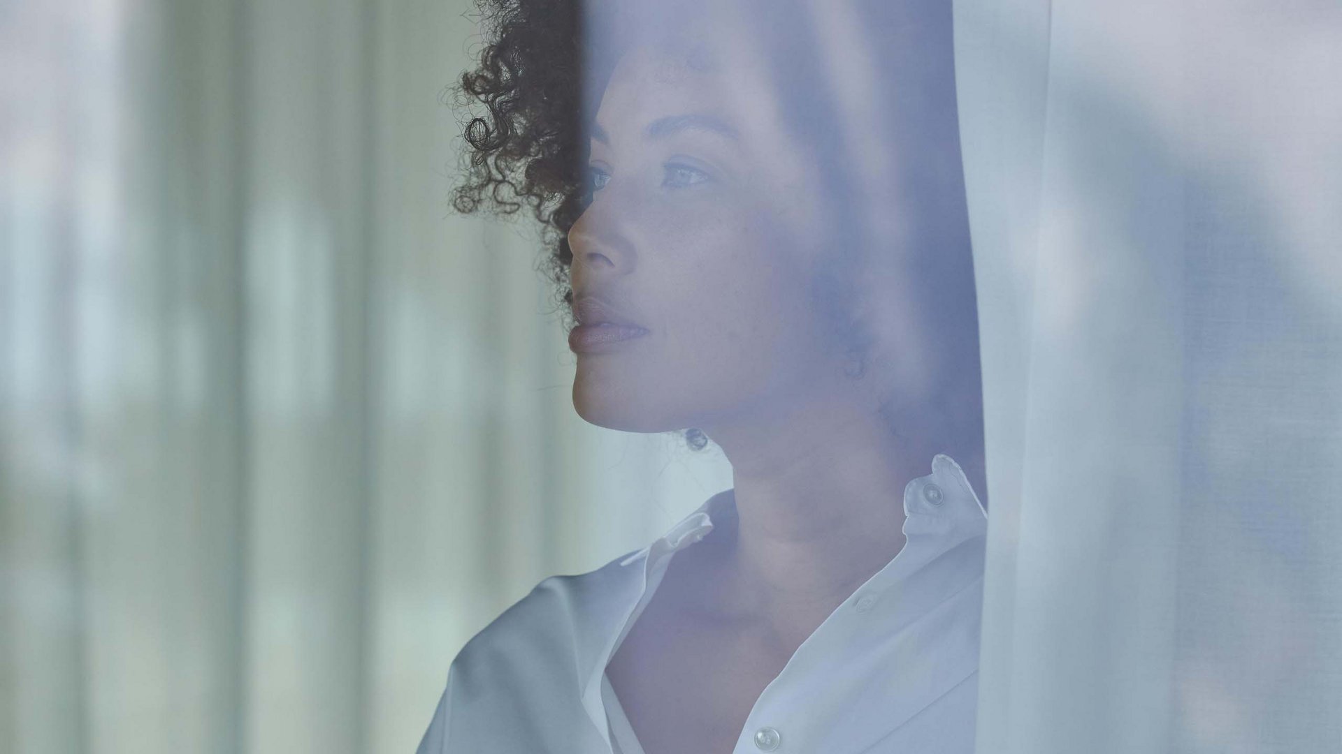 Il tuo hotel in Val Pusteria: Olangerhof Donna con camicia bianca che guarda fuori dalla finestra attraverso una tenda.