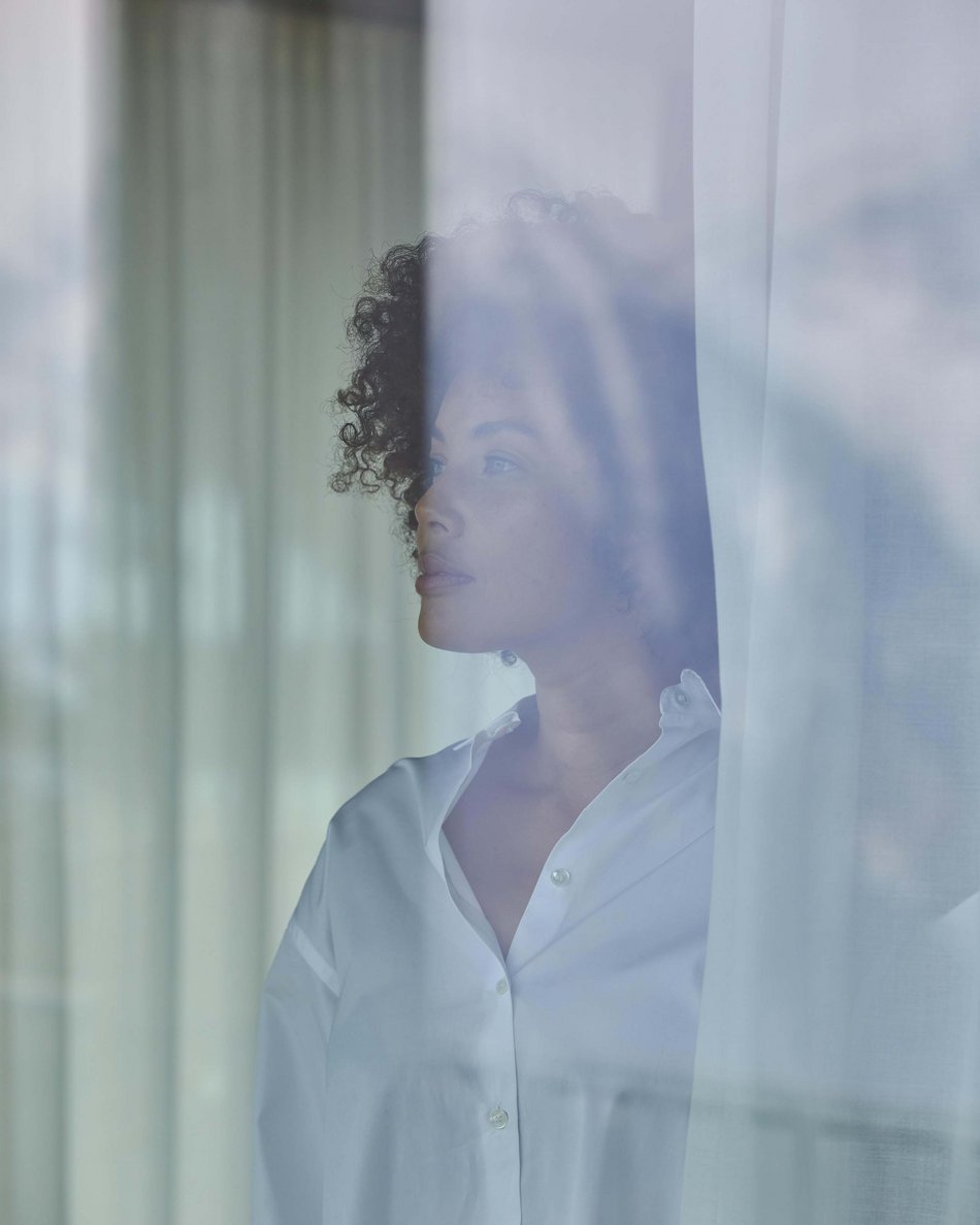 In Olang: a hotel with “Oh”, “Aah”, and “Wow” Woman in white shirt looking out the window through a curtain.