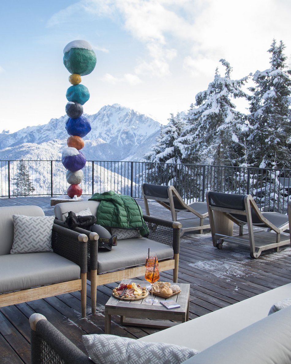 Il tuo hotel in Val Pusteria: Olangerhof Terrazza con divani e snack in montagna innevata con scultura colorata