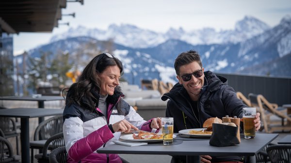 In Olang: a hotel with “Oh”, “Aah”, and “Wow” Couple dining outdoors with snowy mountains in the background.