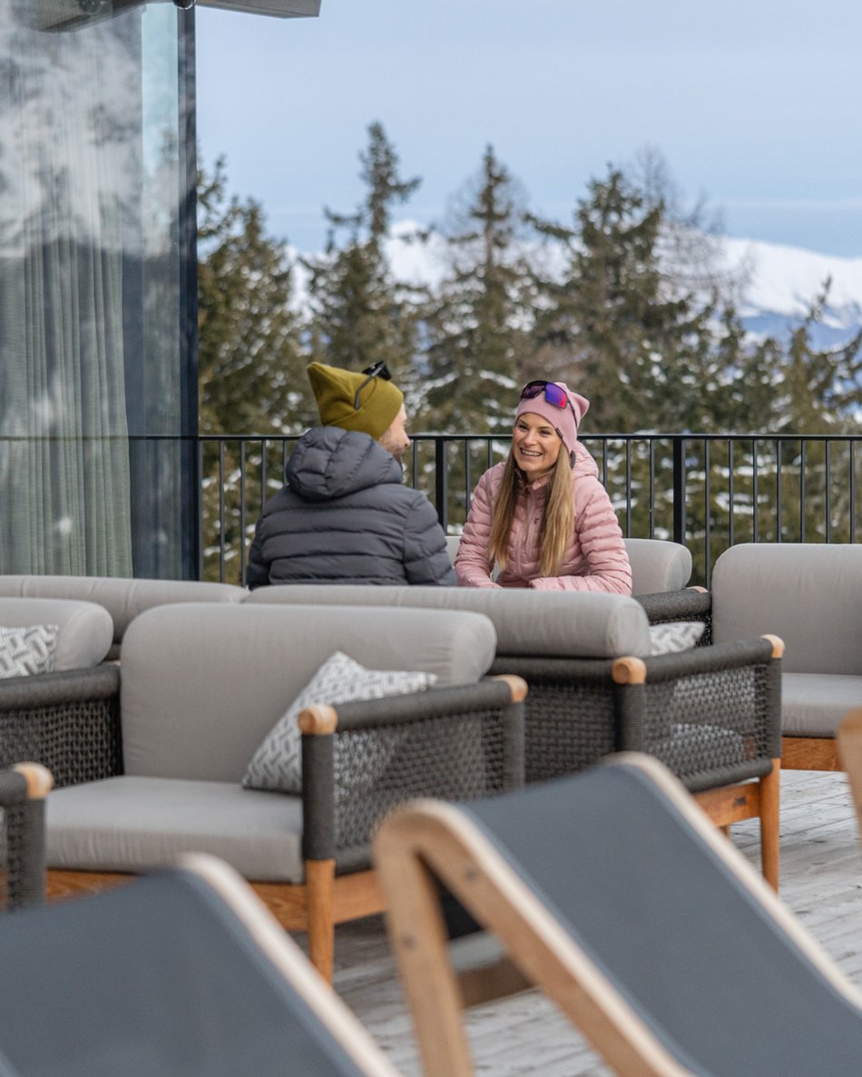 In Olang: a hotel with “Oh”, “Aah”, and “Wow” Couple sitting on lounge chairs on a snowy mountain terrace