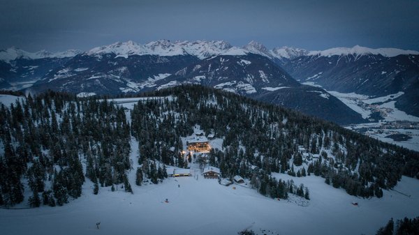 In Olang: a hotel with “Oh”, “Aah”, and “Wow” Lit hotel in snowy landscape with snow-covered mountains in the background at dusk