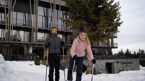 In Olang: a hotel with “Oh”, “Aah”, and “Wow” Two people cross-country skiing in front of a modern building in the snow
