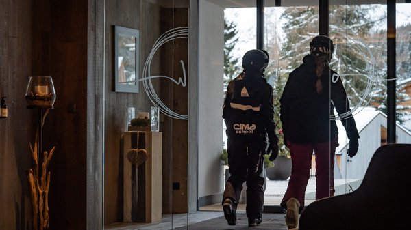 In Olang: a hotel with “Oh”, “Aah”, and “Wow” Two people in ski gear walking out of a building to a snowy landscape.